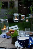 Jam jar lanterns with candles suspended from wire hanging over garden table.
