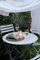 A secluded dining area in the garden made by draping a sheet between rope supports and hanging fairy lights around the edge of the sheeting