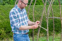 Man tying hazel stick cross bar on with twine to provide stability to tunnel structure