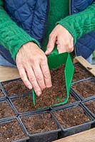 Woman adding a thin layer of compost on top using a green plastic scoop.