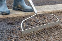 Woman using rake to mix in charcoal soil improver.