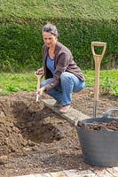 Woman digging in manure into trench. 