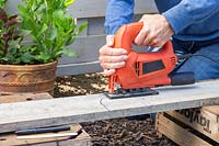 Woman using a jigsaw to cut hole in gravelboard following the marked out shape