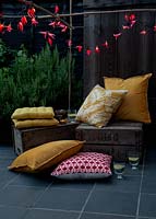 Fairylights decorated with colourful paper shapes to create beautiful decorative outdoor lighting, used here over bamboo cane supports in a seating area with fruit crates and cushions