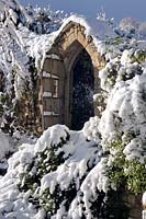 Stone gate in the snow at Burrow Farm Garden, Dalwood, Devon, UK. 