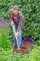 Woman using a fork to dig over an area in the border ready for planting.