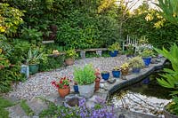 Small pond surrounded by pots and containers in Little Friars Garden, Battle, Sussex, UK. 