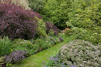 Long terraced borders of flowering perennials and shrubs with grass pathway.
