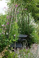 A small table and chairs is enclosed in a rustic arbour smothered in sweet peas.