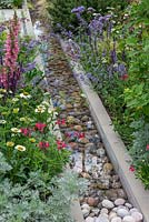 A contemporary water rill filled with large pebbles, and edged in Digitalis, Salvias, Echinacea and Nepeta