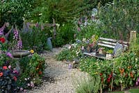 Cottage garden with gravel path winding through relaxed borders of vegetables and flowers. A rustic bench nestles into the planting. BBC Springwatch Garden, designed by Jo Thompson. RHS Hampton Court Palace Garden Festival, 2019. 