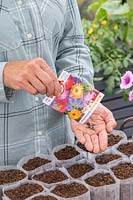 Woman shaking seeds from packet into hand ready for sowing into bio pots.