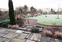Curvaceous lawn framed with borders planted with grasses and evergreens including conifers and hebes at Ellicar Gardens, Doncaster, UK. 