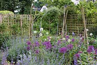 Tiny cottage garden bed planted with Alliums 'Purple Rain', 'Mount Everest' and 'Miami', growing with flowering Nepeta - Catmint.   