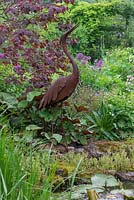 Rusted metal heron stands beside a wildlife pond.