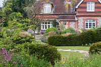 View over wildflowers, fruit trees and lawn enclosed in yew hedges to upper terrace below  flint and brick cottage, originally a farm labourer's dwelling.