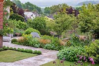 View of the South Downs, over Kingley Vale. Terrace borders of multi-stemmed amelanchiers, geums, hardy geraniums, alliums, euphorbias, Iris 'Rajah', centaureas, aquilegias and roses.