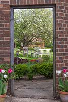 View through brick doorway into back garden with seating area below an old  Worcester Pearmain' apple tree.