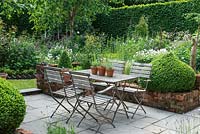 A small paved courtyard with dining table and chairs, flanked by domes of box, overlooks a box parterre planted with Bistort, hardy Geraniums, Centaurea, Foxgloves, ragged robin, Astrantias, Aquilegias and Roses with Silver birches adding height.