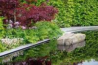 Acer palmatum 'Bloodgood' in a mixed spring border next to a reflective pool with split boulder - The Leaf Creative Garden - A Garden of a quiet contemplation - RHS Malvern Spring Festival 2019