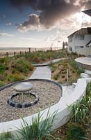 Curved seating around fire pit in seaside garden. 