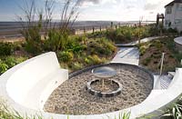 Curved seating around fire pit in sea side garden. 