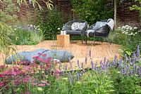 Chairs and cushions on oak decking surrounded by flowerbeds in  Raised by Rivers, RHS Tatton Park Flower Show 2018