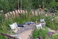 Cushion's on curved dry stone bench backed with timber palisade, in semi wild garden. RHS Hampton Court Festival 2019.