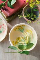 Small bowls made out of salt dough with painted flower imprints, on table with books and fresh flowers