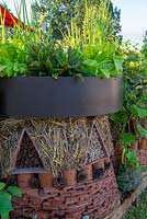 Habitat house made from terracotta tiles, fir cones, bamboo sticks and straw, herbs and salad planted above - Year of Green Action Garden, RHS Hampton Court Palace Flower Festival 2019