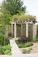 View down path past semi-circular bed towards a wooden pergola topped with annuals