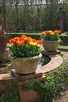 Tulipa 'Monte Orange' and 'Monte Carlo' - Tulips - in containers on plinths around a raised pond