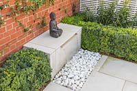 Water feature with sheet of water falling onto pebbles and buddha statue 