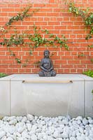 Water feature with sheet of water falling onto pebbles and buddha statue. 