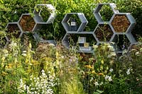 A garden planted to attract wildlife. Contemporary honeycomb shapes feature in a wall designed to be a habitat for insects, especially bees. RHS Hampton Court Palace Garden Festival 2019. Sponsor: Warner's Distillery.