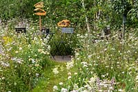 A seating area in a naturalistic garden with wild flowers, providing a habitat for wildlife, birds, insects and bees. RHS Hampton Court Palace Garden Festival 2019.