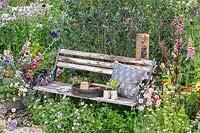 A naturalistic wildlife-friendly garden with a wooden bench and colourful flowers to attract insects including bees. RHS Hampton Court Palace Garden Festival 2019.