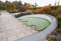Walled garden designed by Brita von Schoenaich featuring a ribbon of grey inlaid slate looping through the space across the central path and over low retaining walls that double as seats. Beds are planted with a mix of shrubs, herbaceous perennials and grasses including persicarias, berberis, asters and Pennisetum orientale framed by hornbeam hedging at Marks Hall Gardens in autumn.