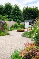 Small garden with water feature, seating area and white garden shed.