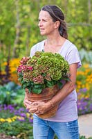 Woman holding a Hydrangea in a pot in a colourful garden