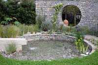 Water feature made from dry stone walling bordered by a gravel path with Stipa tenuissima bordering the pond. Garden: The Harmonious Garden of Life. Sponsor: Mr Robert and Mrs Sue Cawthorn Margheriti Piante, Italy. Chelsea Flower Show 2019.