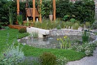 The Harmonious Garden of Life. An environmentally sustainable courtyard with a pond that is kept clean by a reed bed, encircled in clover to enrich the soil. A pergola swingseat is edged in bamboo to purify the air. Sponsors: Mr and Mrs Cawthorn, Margheriti Piante. RHS Chelsea Flower Show 2019.