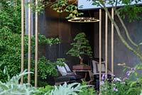 Seating in a garden building with a bonsai tree - The Morgan Stanley Garden, RHS Chelsea Flower Show 2019