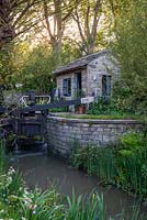 Lock keeper's office next to the lock gates with herbaceous planting of Lupins and Delphiniums - The Welcome to Yorkshire Garden, RHS Chelsea Flower Show 2019