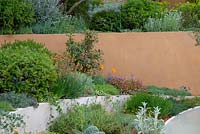 Curved raised beds with mixed planting and orange wall behind - The Dubai Majlis Garden, RHS Chelsea Flower Show 2019.