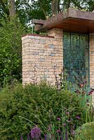 Natural stone building with green roof and water feature and hand-crafted glass panels by Wendy Newhofer, Taxus baccata dome in foreground - The Warner's Distillery Garden, RHS Chelsea Flower Show 2019.