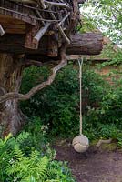 Rope swing for children hanging from tree branch under a tree house - The RHS Back to Nature Garden, RHS Chelsea Flower Show 2019.