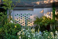 Morning light on The Greenfingers Charity Garden, with mixed planting of Lupinus 'Polar Princess', Lupinus 'Gallery Yellow', Iris and Orlaya grandiflora, Dicksonia antarctica under the walkway - RHS Chelsea Flower Show, 2019.