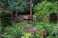 Rusted reclaimed wood oven  with mixed planting of orange and red Geum, Hakenacloa alba aurea, Stipa tenuissima and Taxus baccata hedge - The Walker's Forgotten Quarry Garden, RHS Chelsea Flower Show 2019