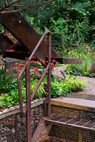 Industrial style rusted steps leading up to a gravel path, through orange and green planting - The Walker's Forgotten Quarry Garden, RHS Chelsea Flower Show 2019